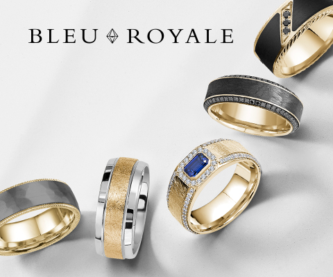 A stylish collection of five Bleu Royale men’s wedding bands displayed on a light gray surface. The rings showcase a variety of bold and modern designs, including combinations of gold, black, and silver tones, with finishes ranging from matte to polished. One standout ring features a vivid blue sapphire centerpiece surrounded by diamonds. The BLEU ROYALE logo is elegantly positioned in black text at the top