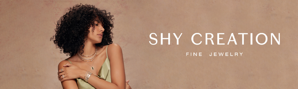 A woman with curly hair wearing layered gold jewelry, including necklaces, rings, and bracelets, poses against a soft beige background. She is dressed in a light green, sleeveless top and looks to the side. The text on the right side reads 