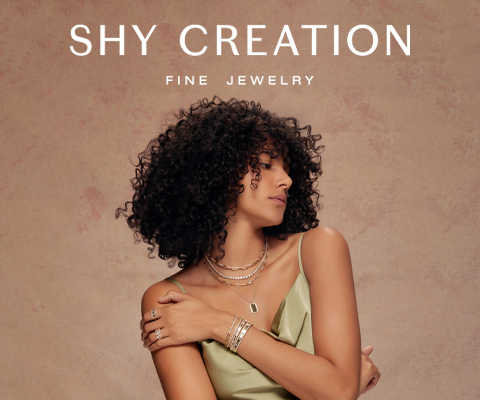 A woman with curly hair wearing layered gold jewelry, including necklaces, rings, and bracelets, poses against a soft beige background. She is dressed in a light green, sleeveless top and looks to the side. The text on the right side reads 