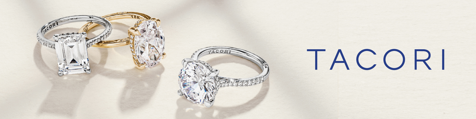 Two elegant diamond engagement rings are displayed on a light surface. The ring on the left features a large emerald-cut diamond set in a platinum band with the brand name 