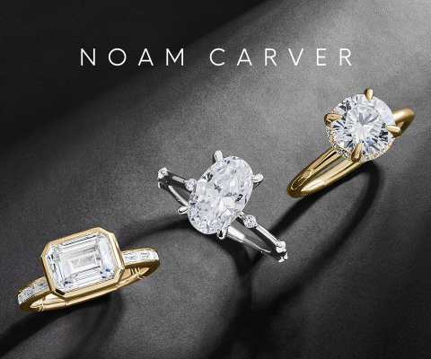 A luxurious display of three Noam Carver engagement rings set against a dark textured background. The rings feature large, brilliant-cut diamonds in different shapes and settings — a rectangular emerald-cut diamond in a yellow gold band with side stones, an oval diamond in a white gold setting with side baguette diamonds, and a classic round brilliant diamond in a yellow gold solitaire setting. The NOAM CARVER brand name is elegantly displayed in white text at the top 