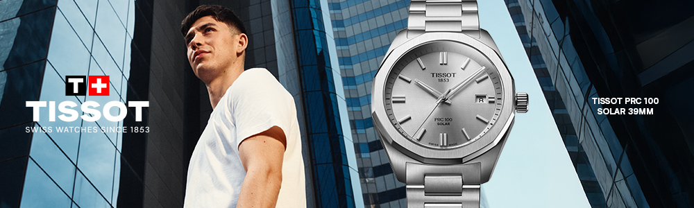 Advertisement for Tissot watches featuring a young man in a white t-shirt standing in front of modern glass skyscrapers. To the right, a close-up of the Tissot PRC 100 Solar 39mm watch is displayed prominently. The watch has a silver metal band and a sleek silver dial with the date shown at the 3 o'clock position. Text on the image includes the Tissot logo with the Swiss flag, the slogan 