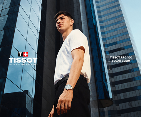 Advertisement for Tissot watches featuring a young man in a white t-shirt standing in front of modern glass skyscrapers. Text on the image includes the Tissot logo with the Swiss flag, the slogan 